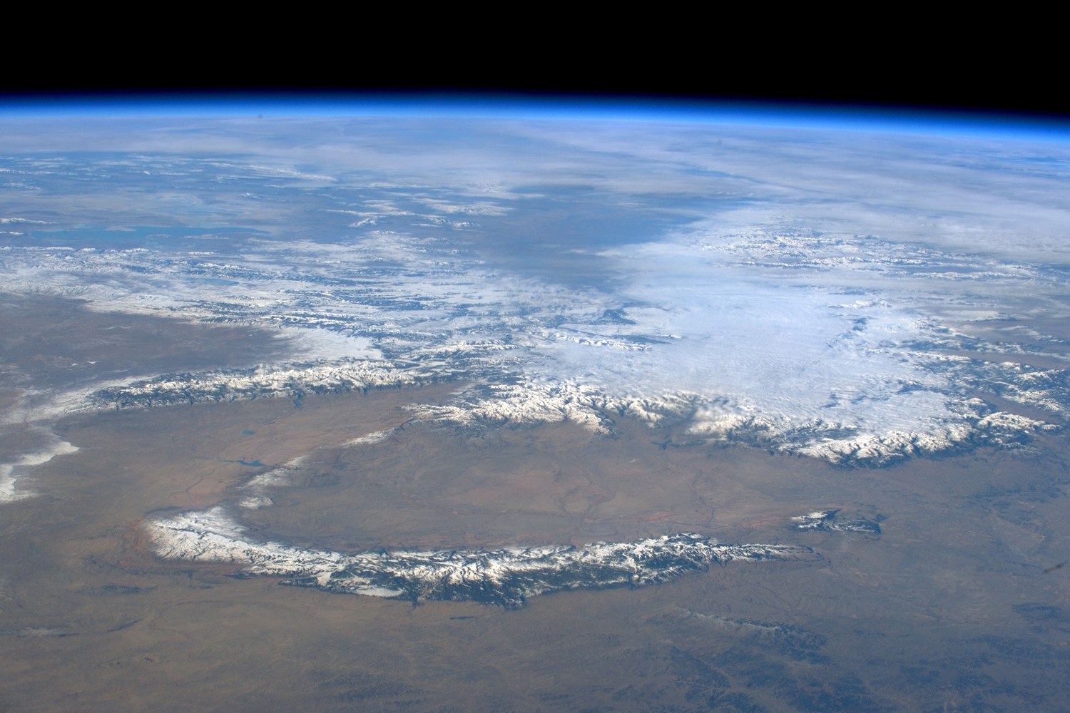 The snow covered spine of the Bighorn Mountains seen from orbit above the brown plains.