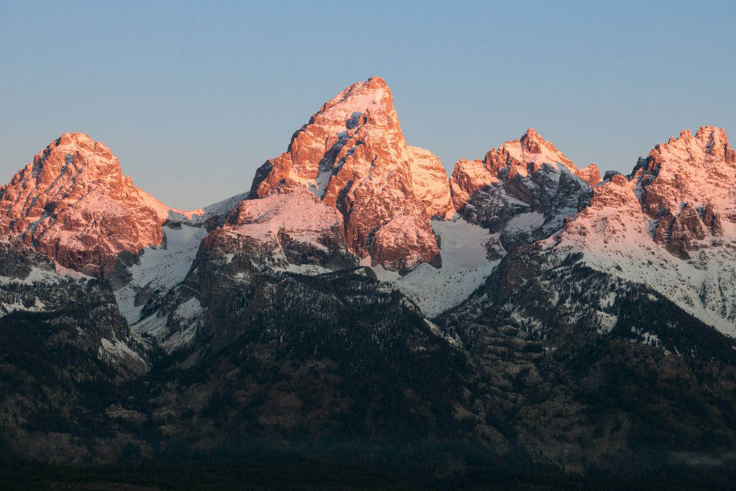 First light turning the summit of Grand Teton and its neighbours pink above shadowed slopes.